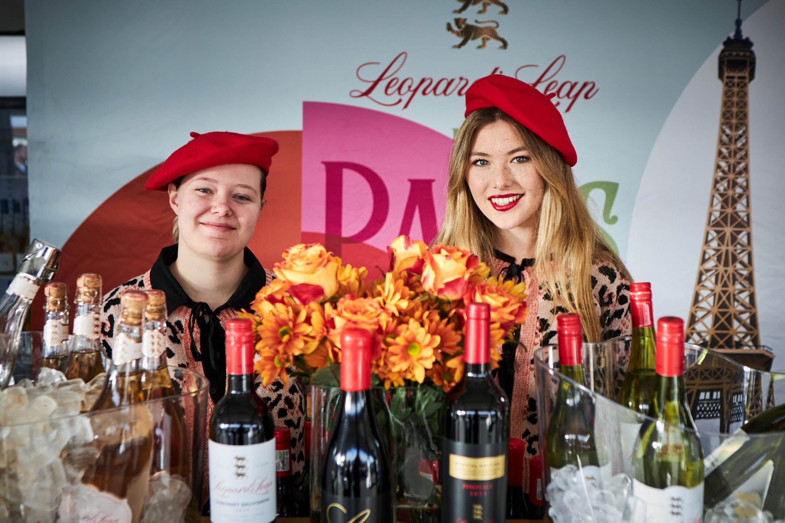 Two women in red berets from Leopard Leap with Eiffel Tower backdrop at the Iconic Franschhoek Bastille Festival