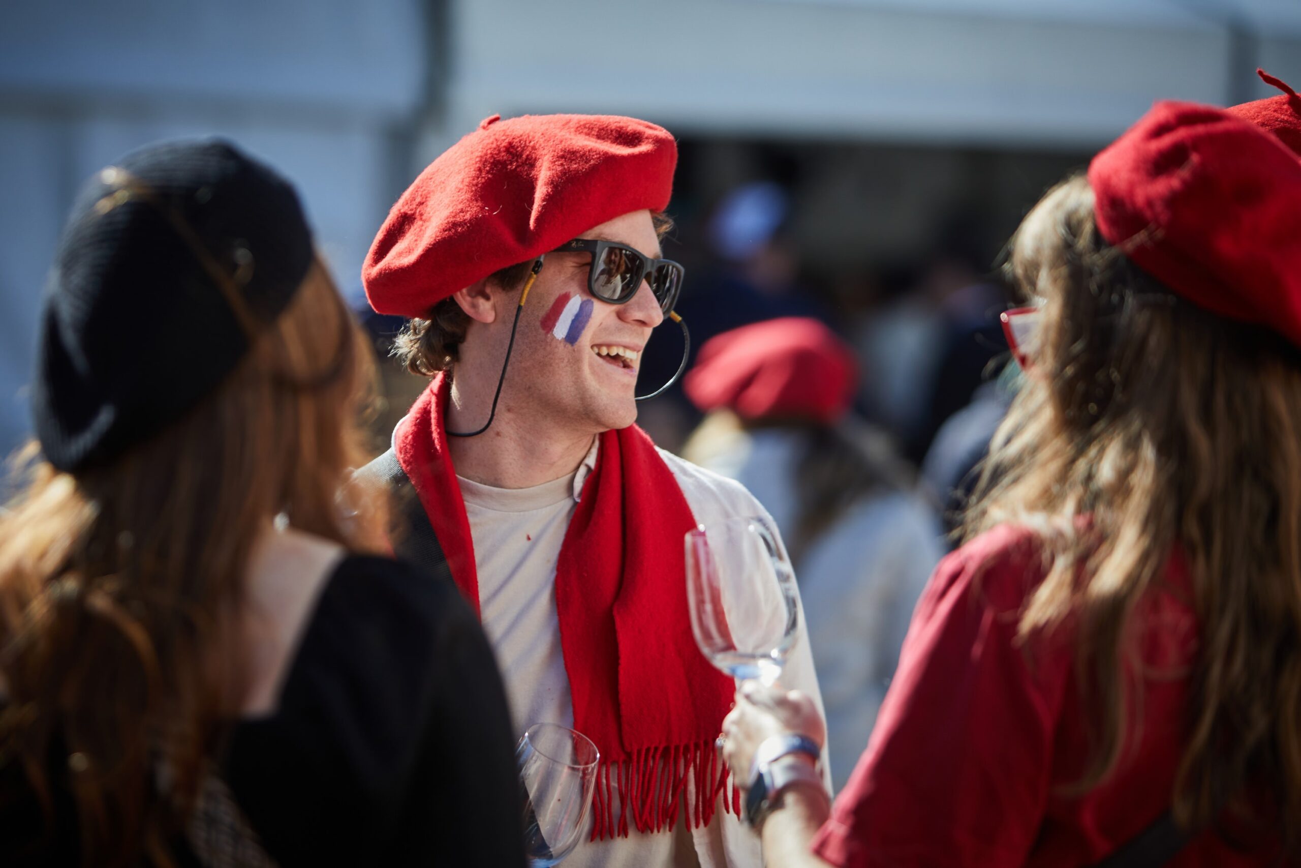 Man in red beret and scarf with French flag face paint laughs with friends
