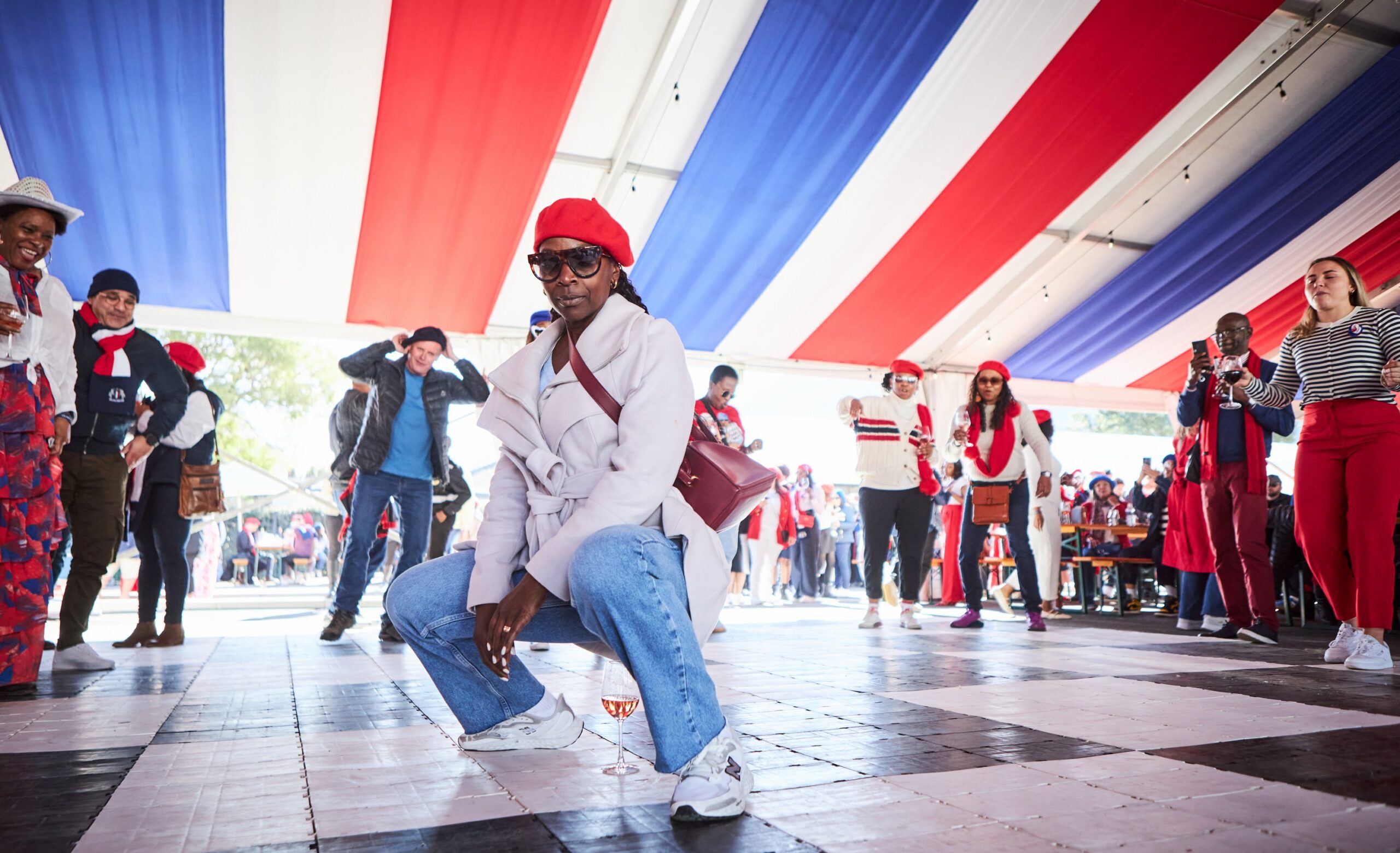 People in red, white, and blue outfits dance under a tent with striped fabric